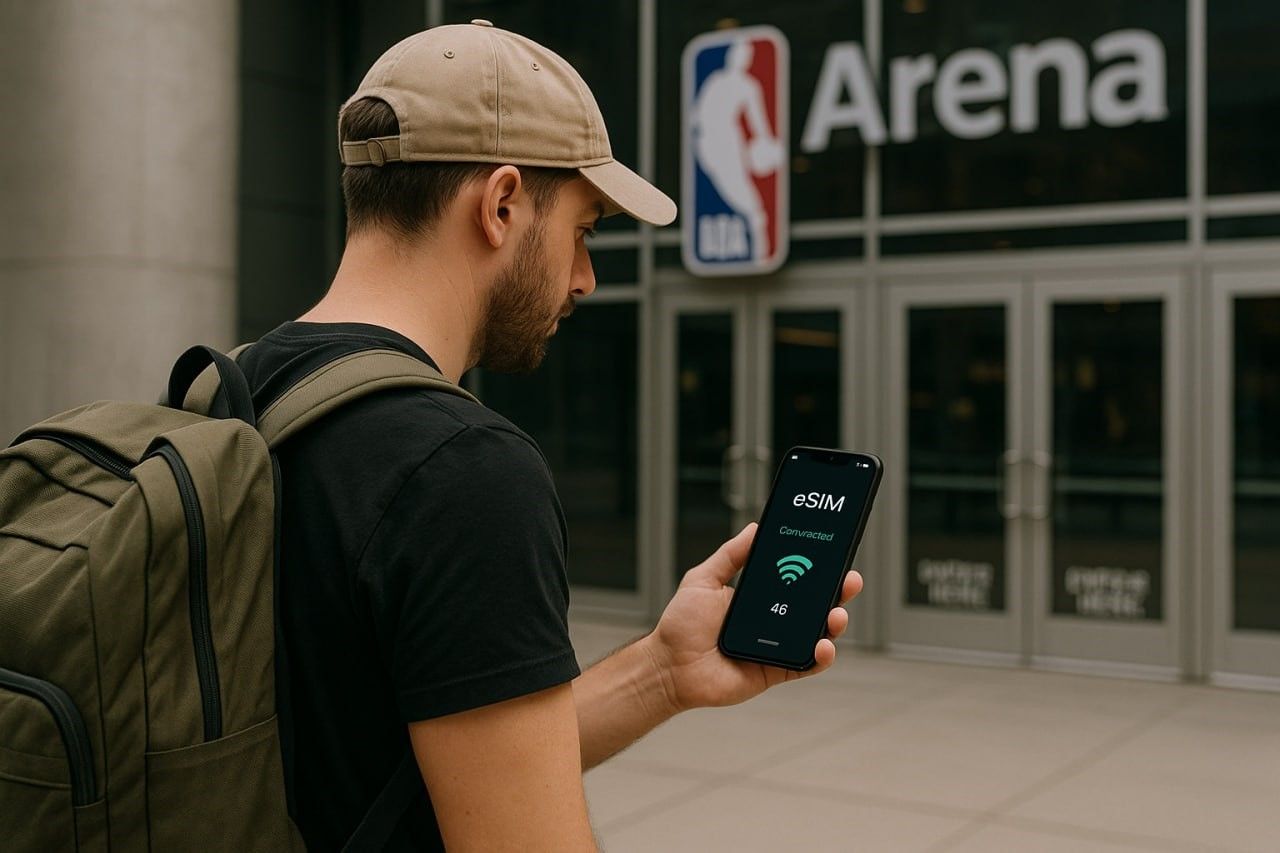 Traveler using smartphone near NBA arena entrance, checking eSIM connection status on screen