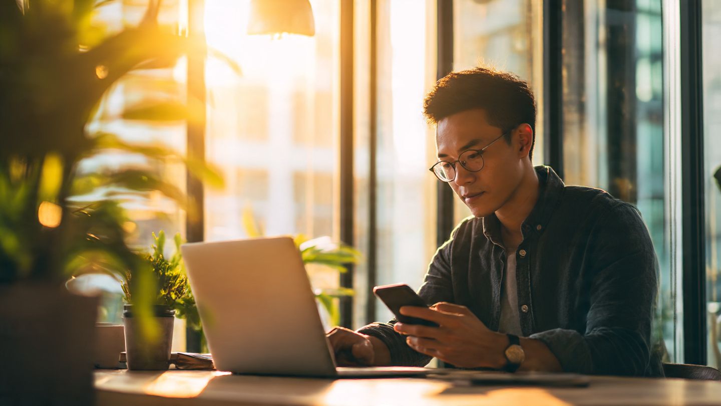 A business professional working on a laptop in a Singapore coworking space while checking eSIM data usage on a smartphone; warm daylight tones; theme of Asia Pacific connectivity