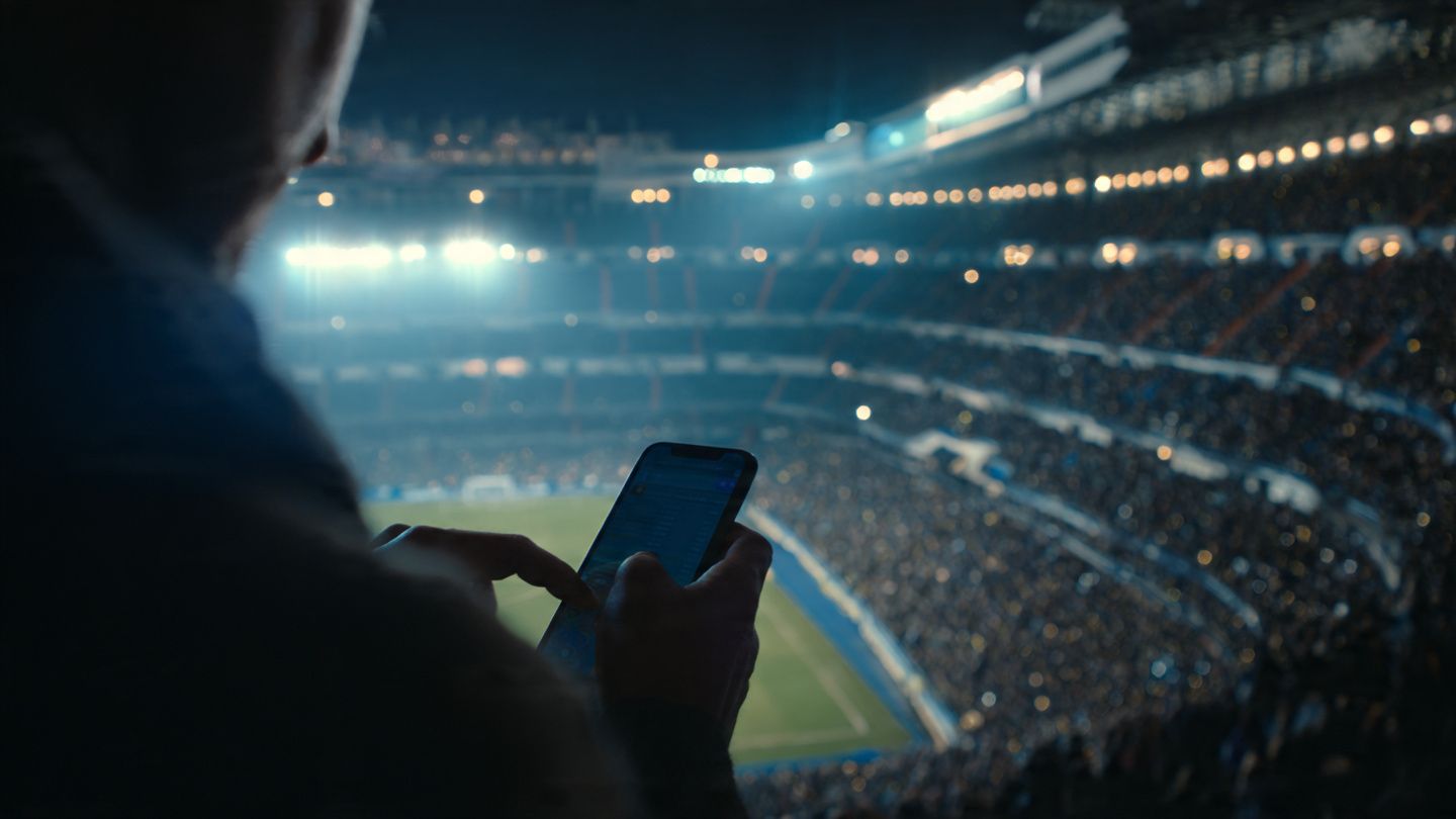 A close-up of a traveler activating an eSIM on their smartphone while overlooking the Santiago Bernabéu stands, with bright stadium lights and fans forming a dynamic atmosphere; crisp documentary style