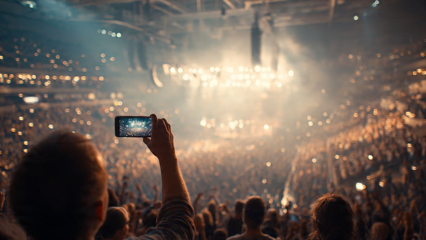A concertgoer holding a lit-up smartphone among a crowd inside an arena, dynamic lighting, instructional and atmospheric travel style