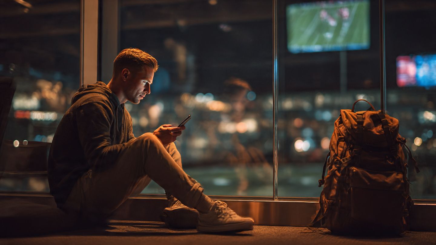 Traveler watching NFL highlights on a phone at an airport lounge, bright travel vibes, modern tech, excitement for sports streaming abroad