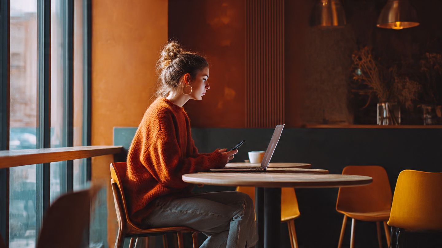 A digital nomad sitting in a café with a laptop and smartphone, warm tones, modern interior, used to illustrate the ease of activating an eSIM while traveling