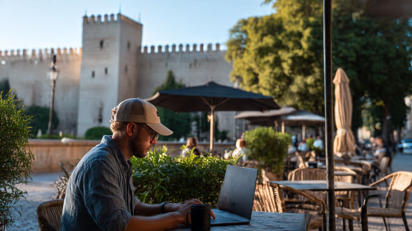 A digital nomad working on a laptop at an outdoor café in Zaragoza with the Aljafería Palace in the background, illustrating seamless eSIM connectivity; modern, lifestyle editorial style