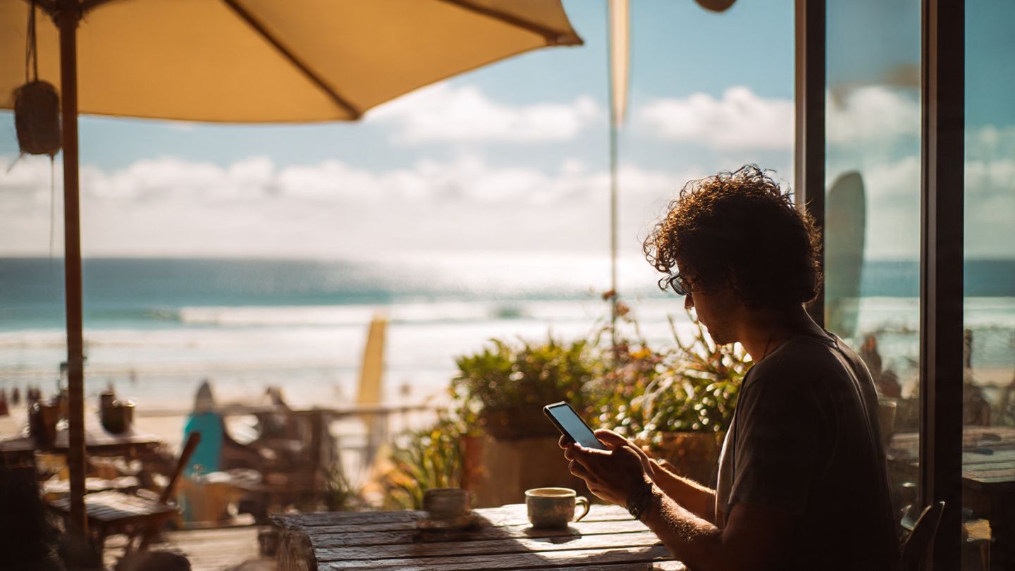 A traveler at a beachside Australian café installing an eSIM on their smartphone, with sunlight, relaxed atmosphere, and digital-travel aesthetic