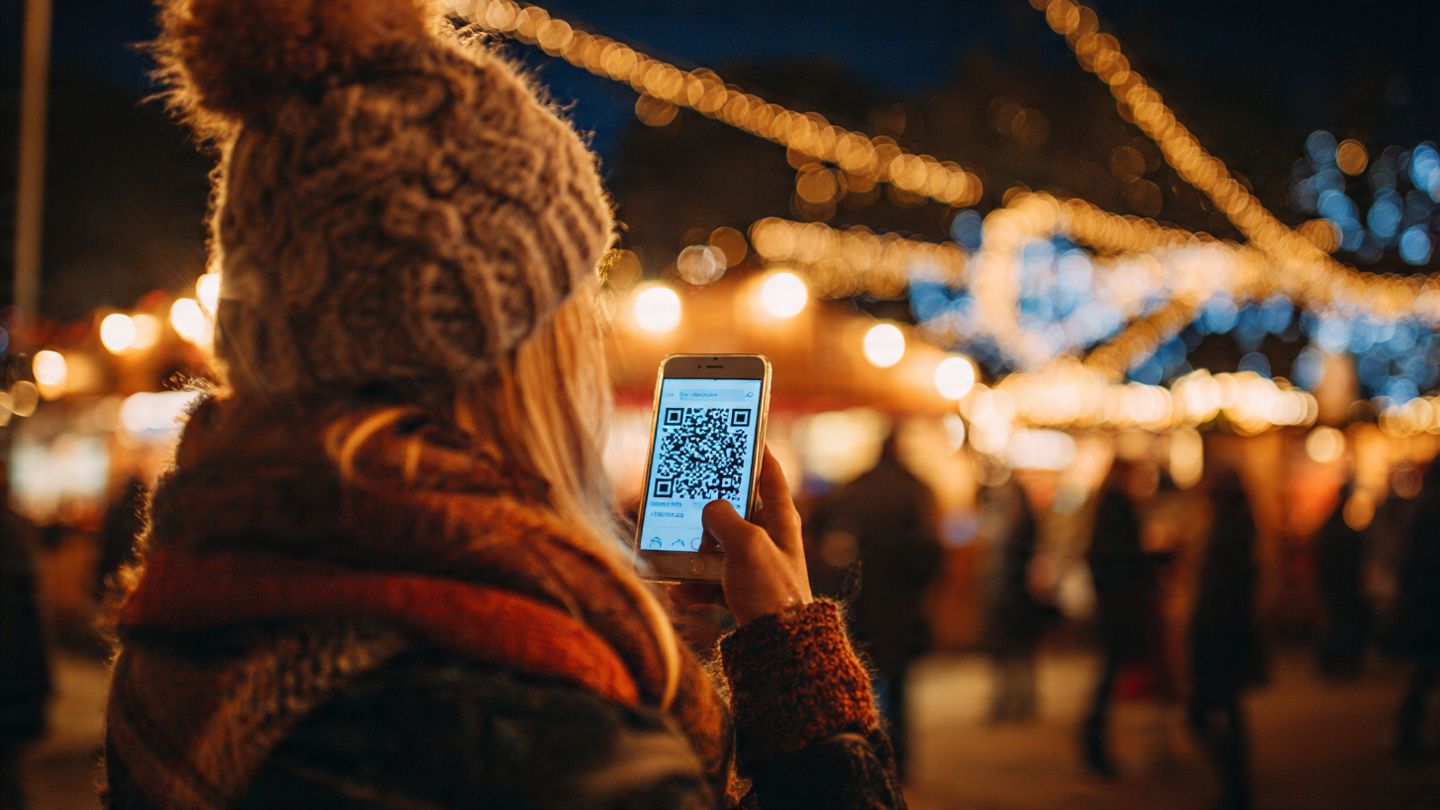 A traveler holding a hot drink while scanning an eSIM QR code at a German Christmas market, festive lights glowing, with a warm and cozy holiday travel vibe