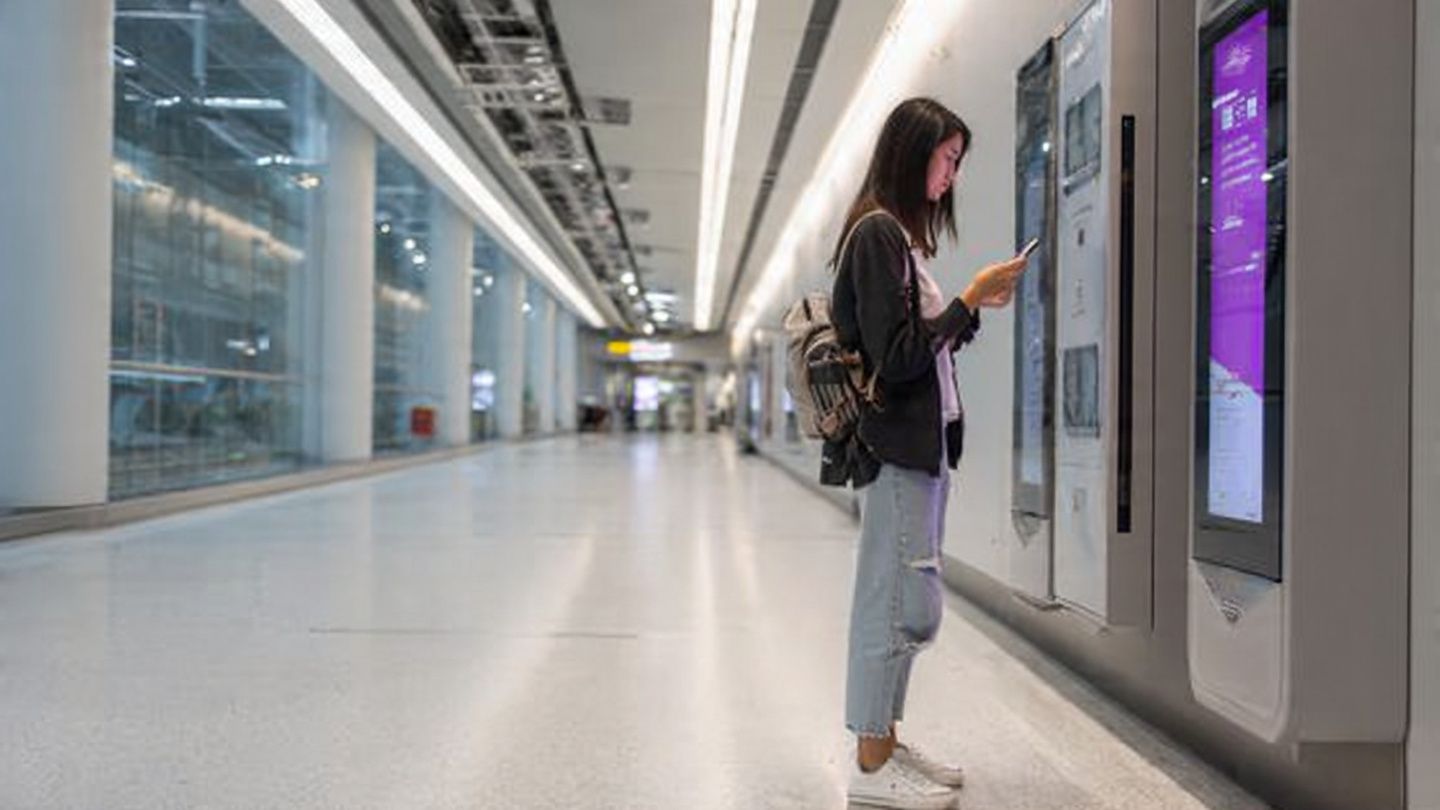 A traveler installing an eSIM on their smartphone inside Hong Kong International Airport, bright modern terminal, instructional layout