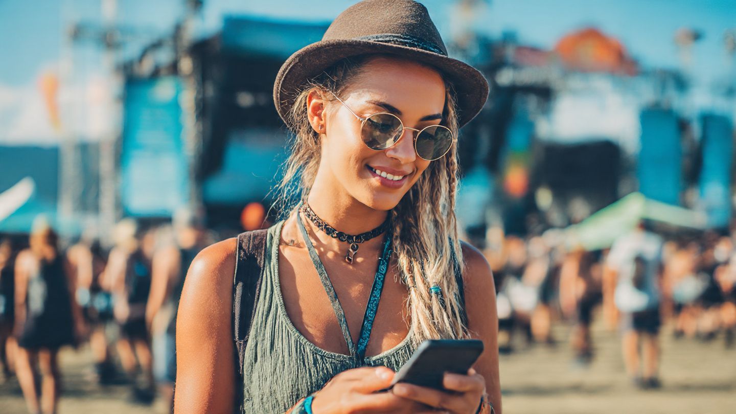 A traveler outdoors at a music festival scanning a mobile ticket on their smartphone using reliable data connectivity; vibrant, energetic editorial event photography
