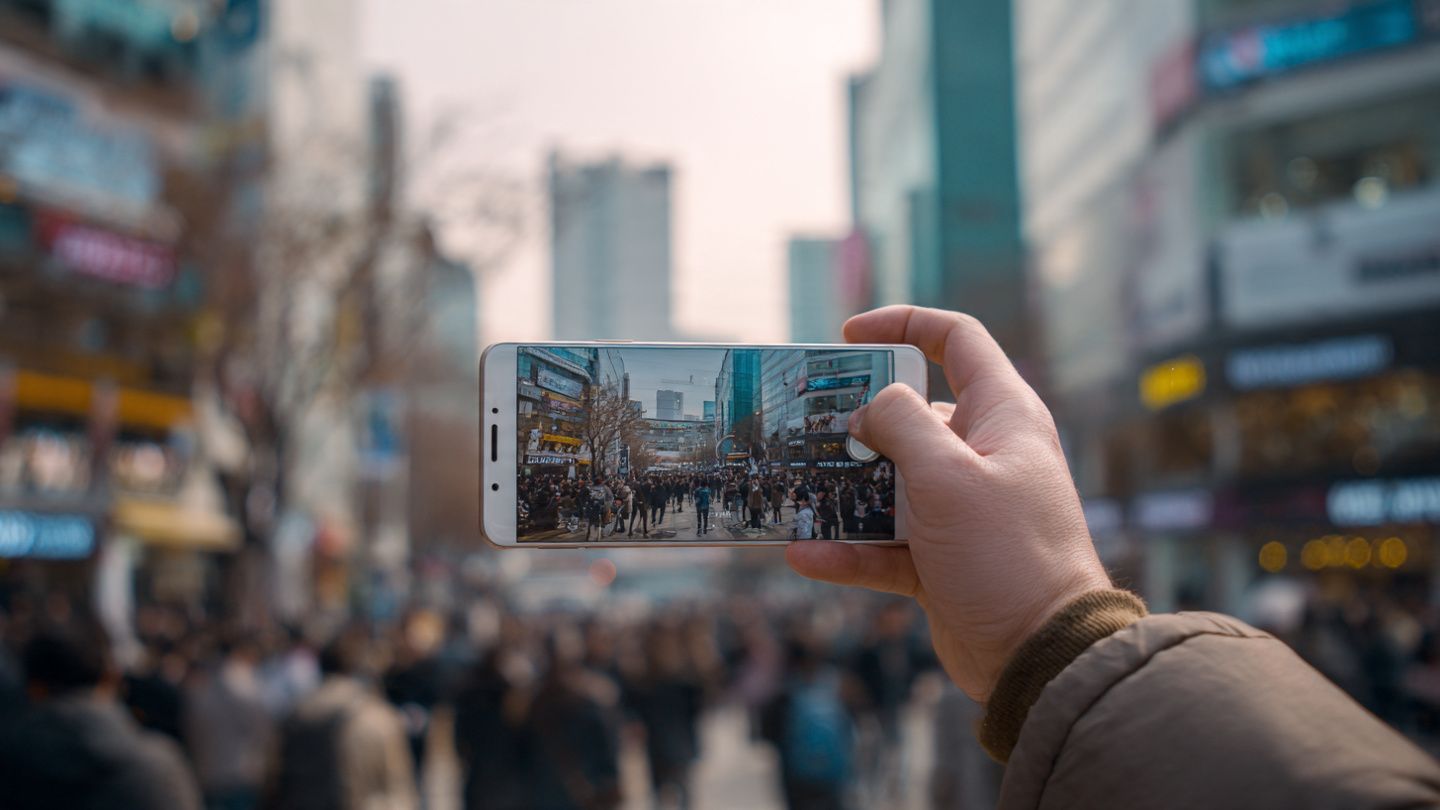A traveler photographing K-drama filming locations using a smartphone, soft cinematic tones, urban Seoul background, lifestyle travel documentation