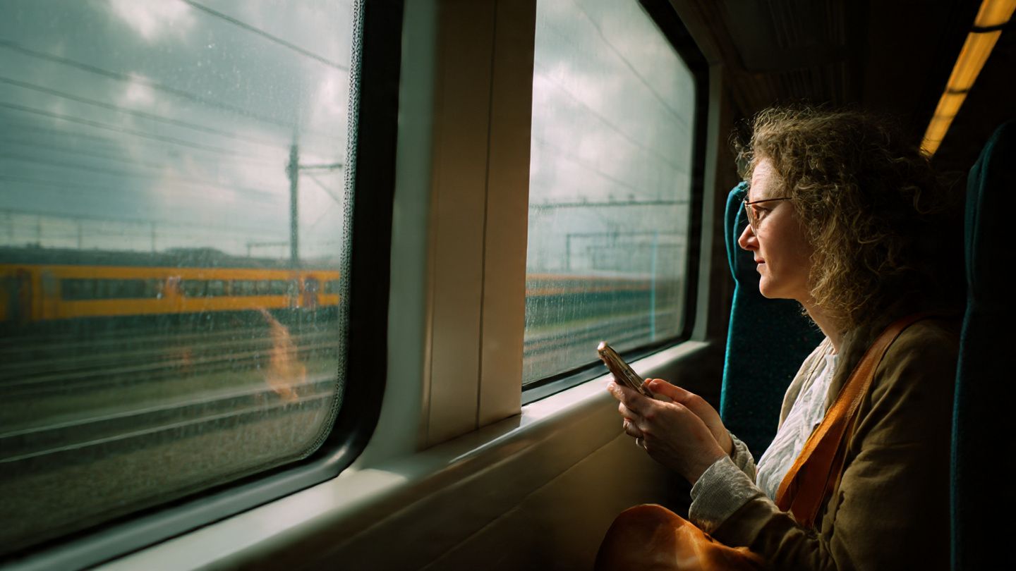 A traveler riding a train from Schiphol Airport toward Amsterdam Central Station while using a smartphone to check maps; crisp documentary-style travel imagery