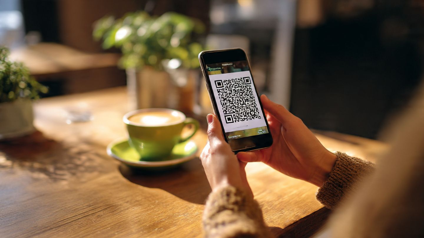 A traveler scanning a QR code on a smartphone in a cozy café before heading to a music festival — lifestyle tech setup scene