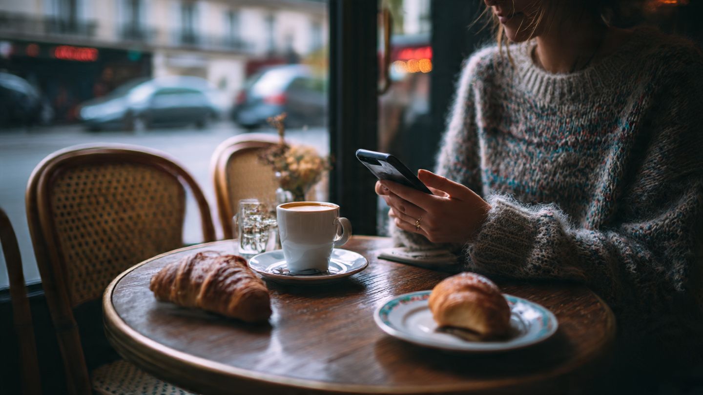 A traveler sitting at a Paris café installing an eSIM on their smartphone; cozy lifestyle aesthetic with focus on simple tech setup