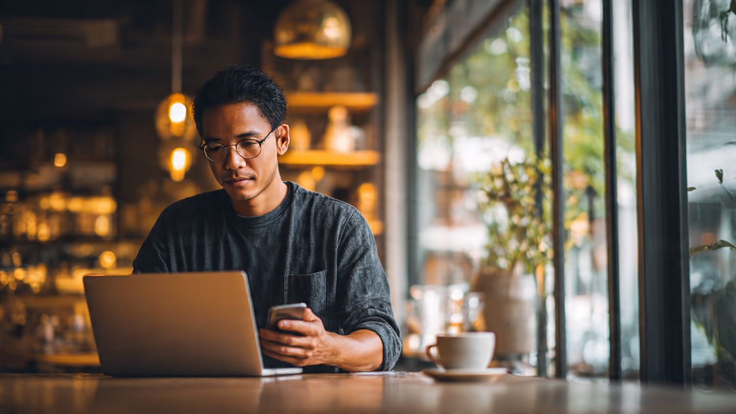 an entrepreneur working in a café in Singapore on a laptop using mobile data, visualizing cross-border connectivity