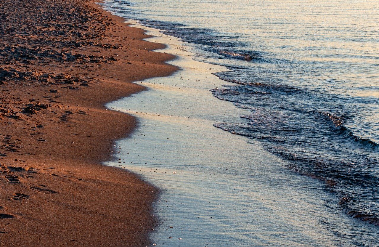 A serene sandy shoreline with gentle waves meeting the beach at sunset.