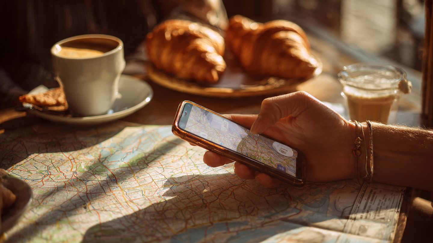 Close-up of a traveler setting up an eSIM on a smartphone at a Paris café; warm daylight, lifestyle-travel tone, with croissants and a metro map in the background