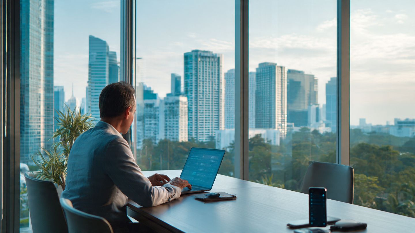 Corporate traveler working on a laptop inside a Singapore meeting room with skyline view, smartphone showing active eSIM data line, modern professional tone