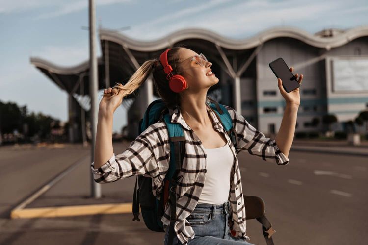 Happy traveler girl listening to music and using smartphone outdoors