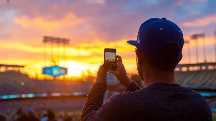 A baseball fan taking a selfie outside Dodger Stadium in Los Angeles at sunset, vibrant colors, travel lifestyle photo