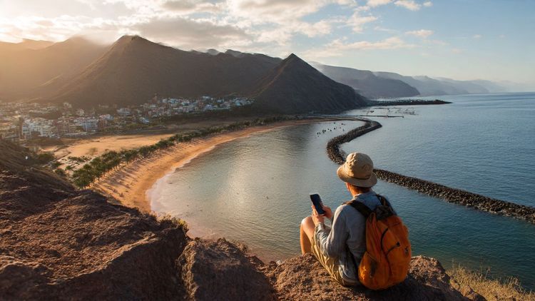 A bright Canary Islands coastal scene with a traveler holding a smartphone near Playa de las Teresitas, warm sunlight, holiday energy, demonstrating mobile connectivity during a Tenerife trip.