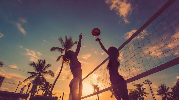 A professional beach volleyball player spiking the ball on a tropical beach during sunset, capturing the energy and athleticism of global tournaments. Vibrant, travel-lifestyle photo.