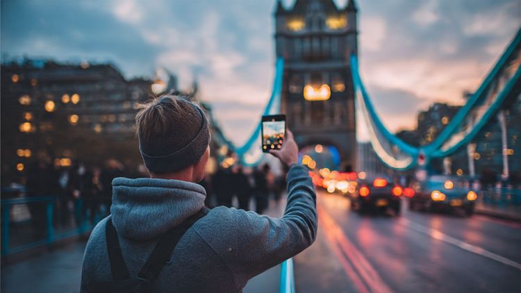 A traveler at London’s Tower Bridge taking a selfie, phone in hand, showing a strong 5G signal — bright, energetic, and modern travel aesthetic