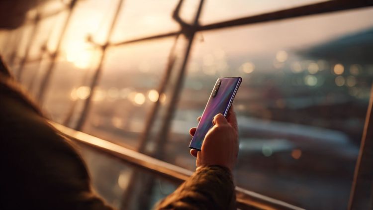 A traveler holding an OPPO Find X9 Pro against an airport window, warm lighting, cinematic style, showcasing mobile setup for international eSIM activation