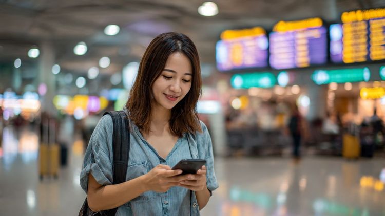 A traveler in Kuala Lumpur airport scanning their phone while comparing eSIM plans; bright, friendly, informative style
