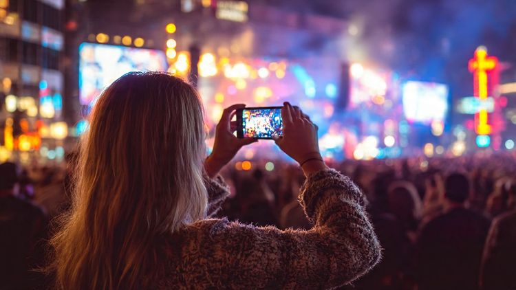 A traveler in Nashville taking photos of a live country music concert at night, vibrant lights, festive atmosphere — travel photography style