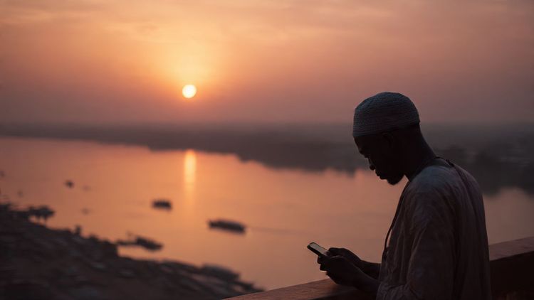 A traveler overlooking the Niger River in Bamako at sunset while checking their phone; warm, documentary-style photograph capturing West Africa connectivity needs