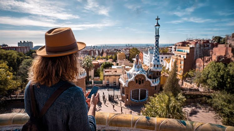 Golden-hour view of Málaga’s port and Alcazaba fortress with a traveler checking their phone; cinematic, warm, travel-journal style