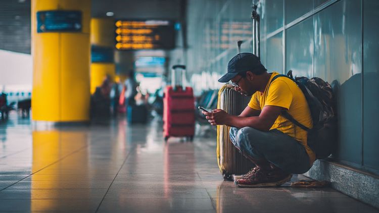 A traveler using a smartphone at Dhaka Airport, checking maps online while waiting for luggage — vibrant, modern travel photography for connectivity theme