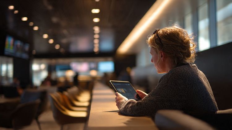A traveler watching German TV on a tablet at an airport lounge — bright, modern lighting, focus on streaming screen, connected through eSIM