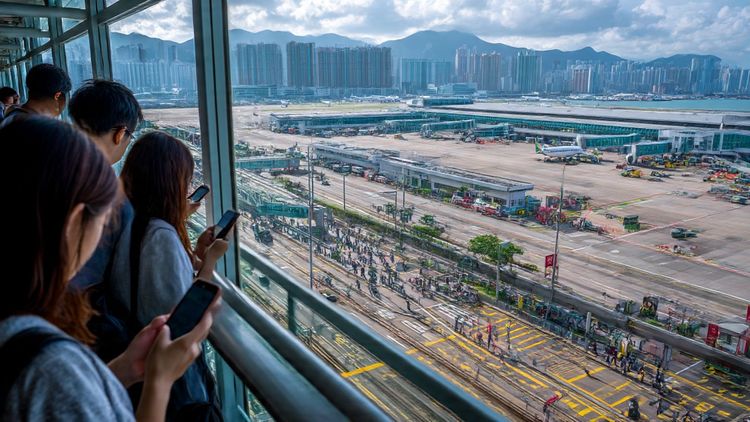 Aerial view of Hong Kong’s Kai Tak area with travelers using smartphones; bright, modern, travel-focused scene