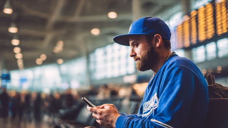 Baseball fan at an airport watching MLB highlights on a smartphone – bright, travel-ready vibe, connection and excitement in the air