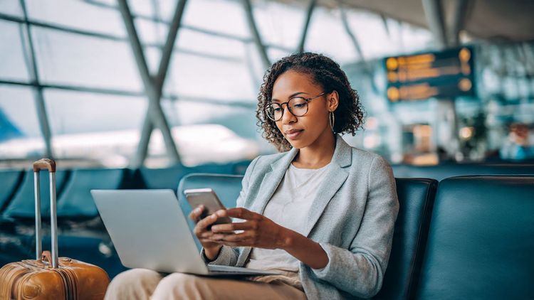Business traveler in airport lounge working on laptop and phone; calm professional tone; purpose: illustrate seamless global connectivity during international business travel