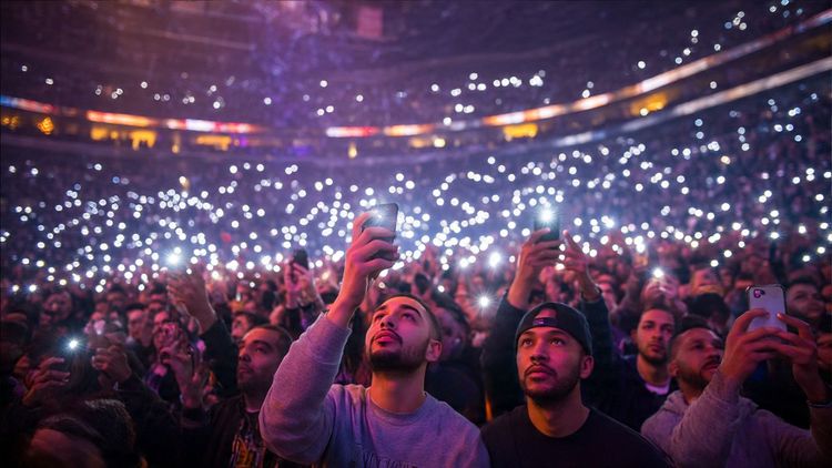 Crowd of NBA fans at All-Star Weekend taking photos with their phones – vibrant arena lights, celebration atmosphere, digital connectivity theme