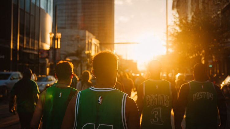 Fans in green Celtics jerseys walking through downtown New Orleans near the Smoothie King Center, captured during sunset — vibrant, travel photography for sports tourism blog