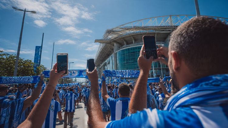 Fans outside Estádio do Dragão in Porto, waving blue and white FC Porto scarves, capturing videos on smartphones — vibrant match-day atmosphere, sunny afternoon.