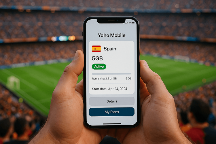 A fan holding a smartphone showing the Yoho Mobile app with a Spain data plan active inside the Camp Nou stadium during a match.