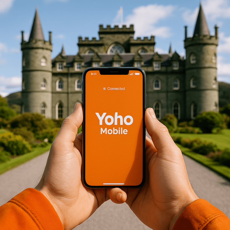 A traveler holds a smartphone with the Yoho Mobile app open, showing good signal in front of Inveraray Castle, Scotland.