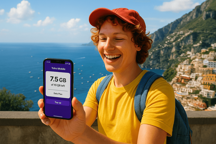 A traveler smiling while checking their remaining Yoho Mobile eSIM data on their phone, with the beautiful Italian coast in the background.