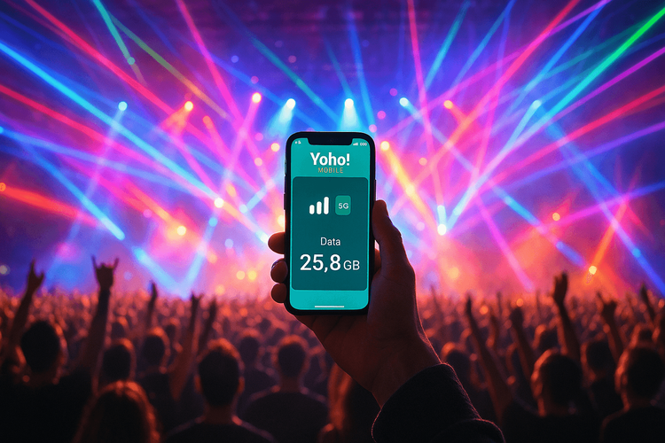 A fan at a concert holding a smartphone with the Yoho Mobile app showing a strong connection.