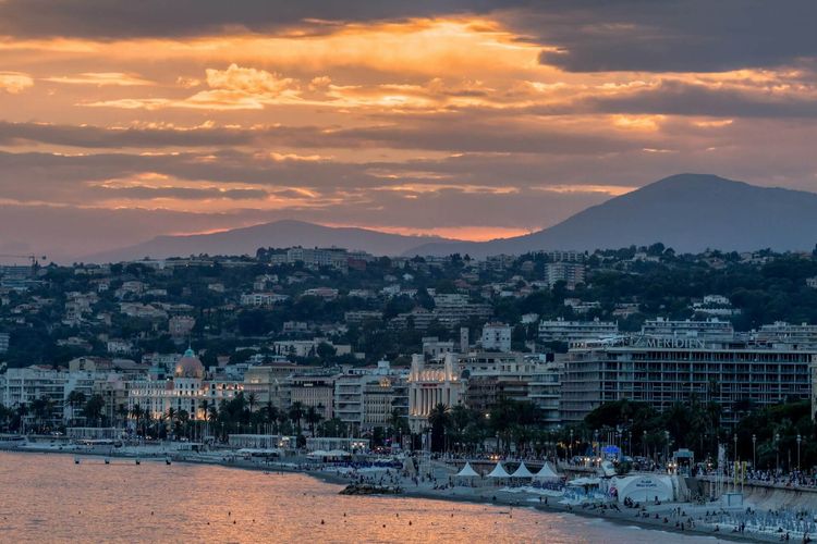 Sunset over Nice with a skyline of hills and city lights reflecting on the water
