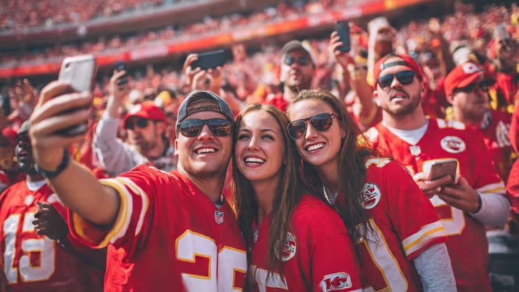 Scene of NFL fans wearing Kansas City Chiefs jerseys at Arrowhead Stadium, taking selfies and using smartphones; dynamic crowd atmosphere, red and gold tones; purpose: illustrate connected NFL travel experience