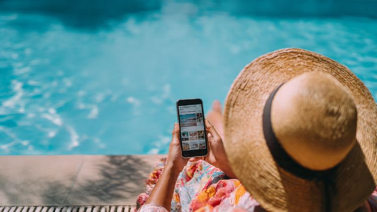 Traveler relaxing by a pool with a smartphone open to entertainment news apps – tropical vacation setting, bright and cheerful tone, focus on connectivity.