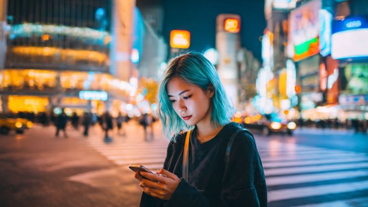 Traveler using a smartphone in Shibuya Crossing, Tokyo, enjoying fast eSIM internet access — bright city lights, modern vibe, connectivity theme.