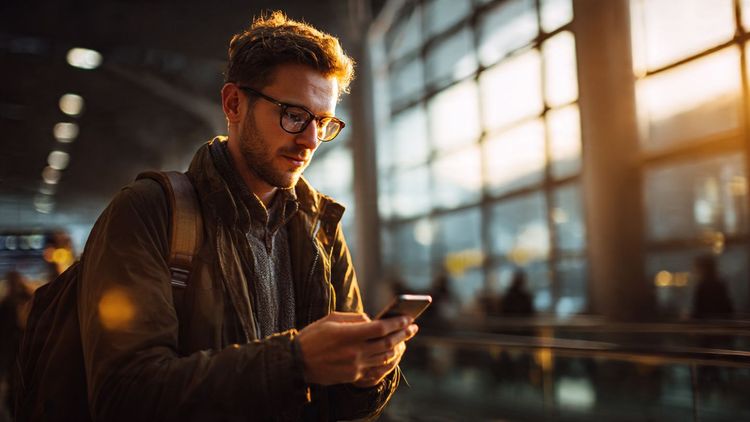 Traveler using smartphone at airport, focusing on digital security and eSIM connectivity, warm natural lighting