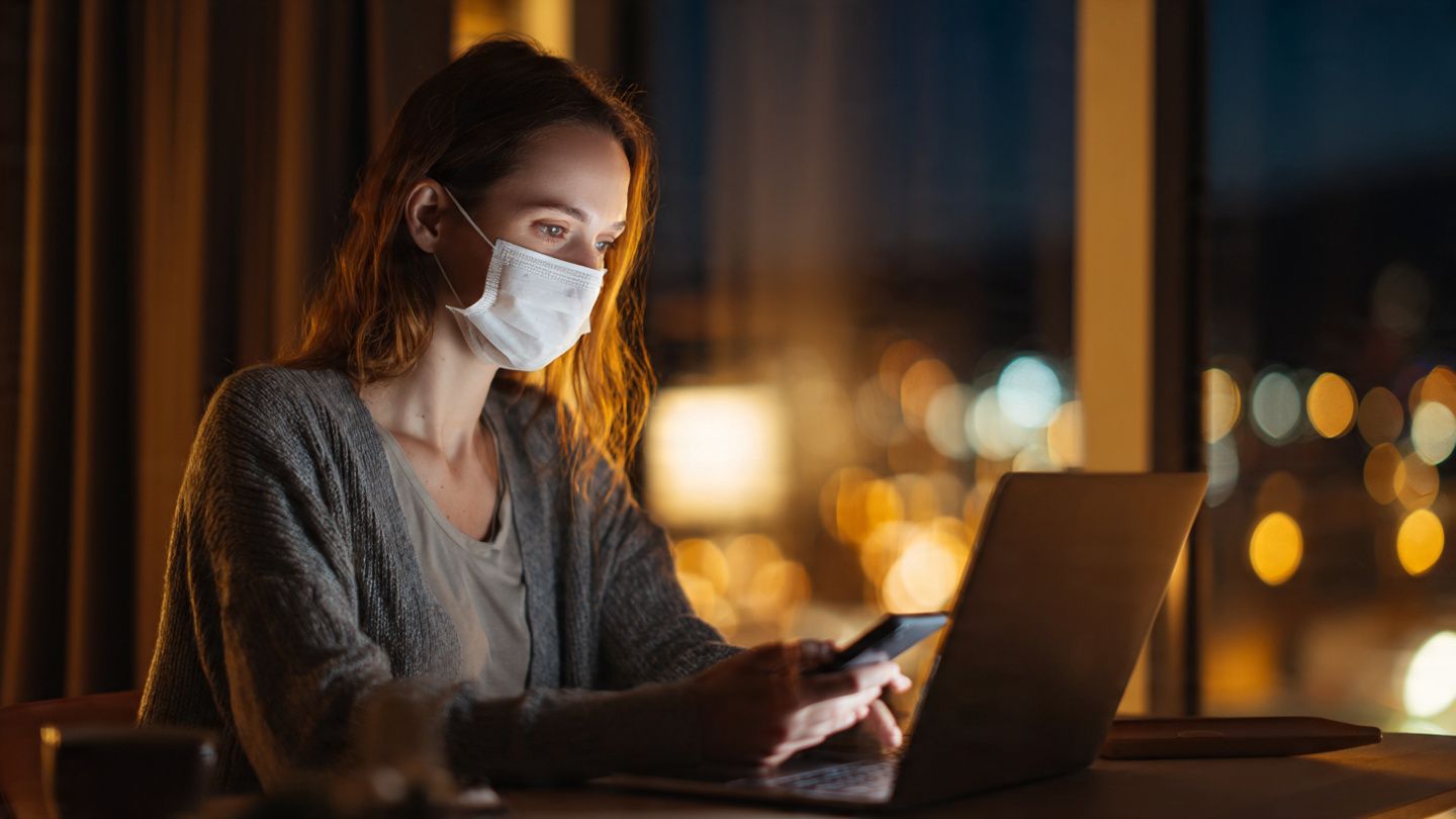 Traveler at a hotel desk using a laptop and smartphone to complete health forms during a pandemic alert; soft evening lighting; crisis preparedness aesthetic