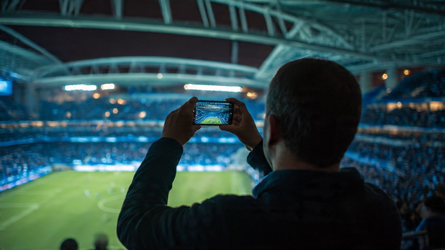 Traveler inside Estádio do Dragão stadium stands, filming FC Porto’s pre-match warm-up using smartphone — energetic sports atmosphere, night lighting, fan crowd.