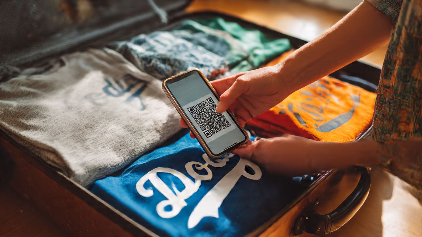 Traveler scanning a QR code for eSIM activation on a smartphone while packing LA Dodgers merchandise in a suitcase — bright, lifestyle photography capturing travel preparation energy