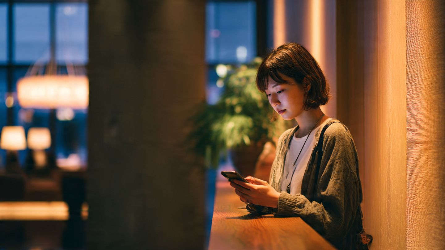 Traveler scanning a QR code on their phone to activate an eSIM in a hotel lobby in Kobe — cozy indoor light, calm preparation for sightseeing